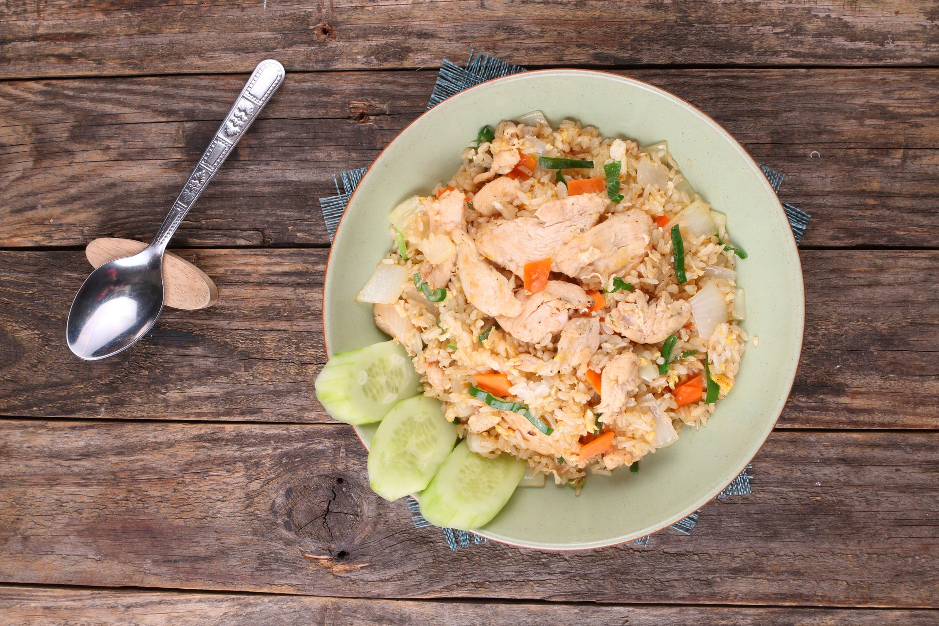 Top view of chicken fried rice with vegetables on rustic wooden table for a cozy meal setting.