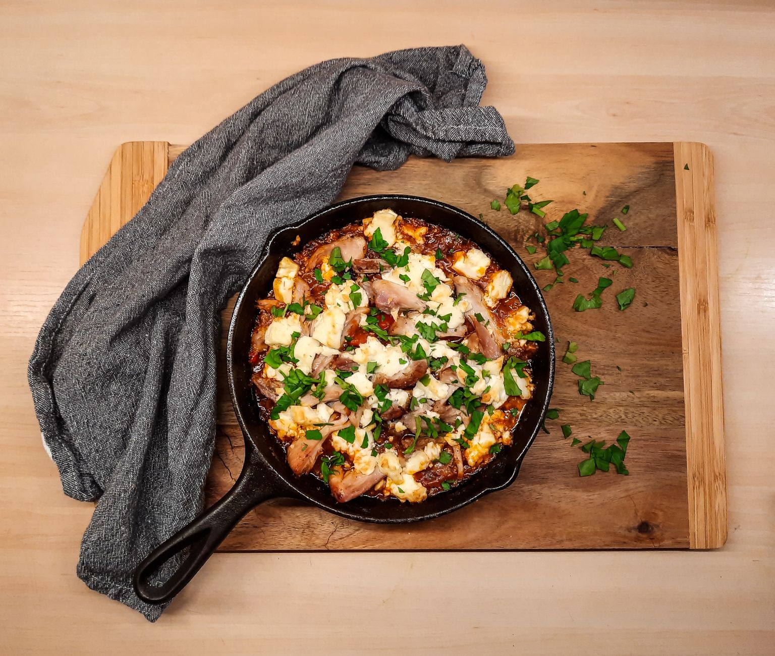 Top view of a homemade chicken skillet dish garnished with fresh herbs on a wooden board.