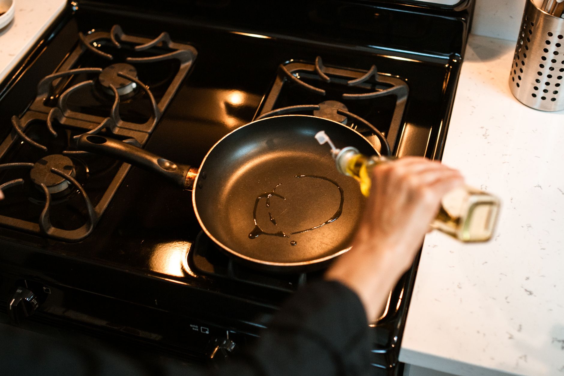 From above crop faceless chef pouring olive oil into frying pan on stove while cooking at home