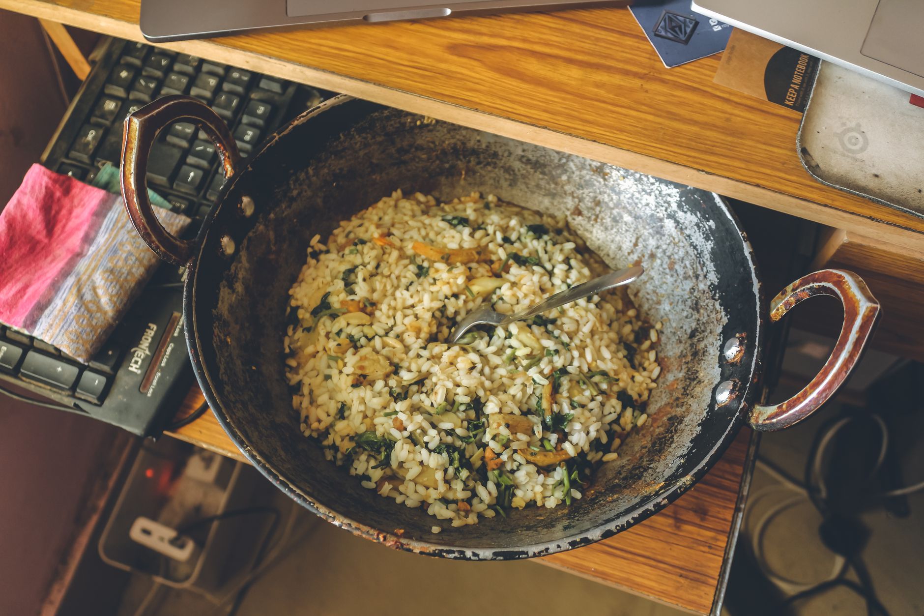 Top view of a cooked rice dish in a rustic pan on a wooden table with a keyboard nearby.
