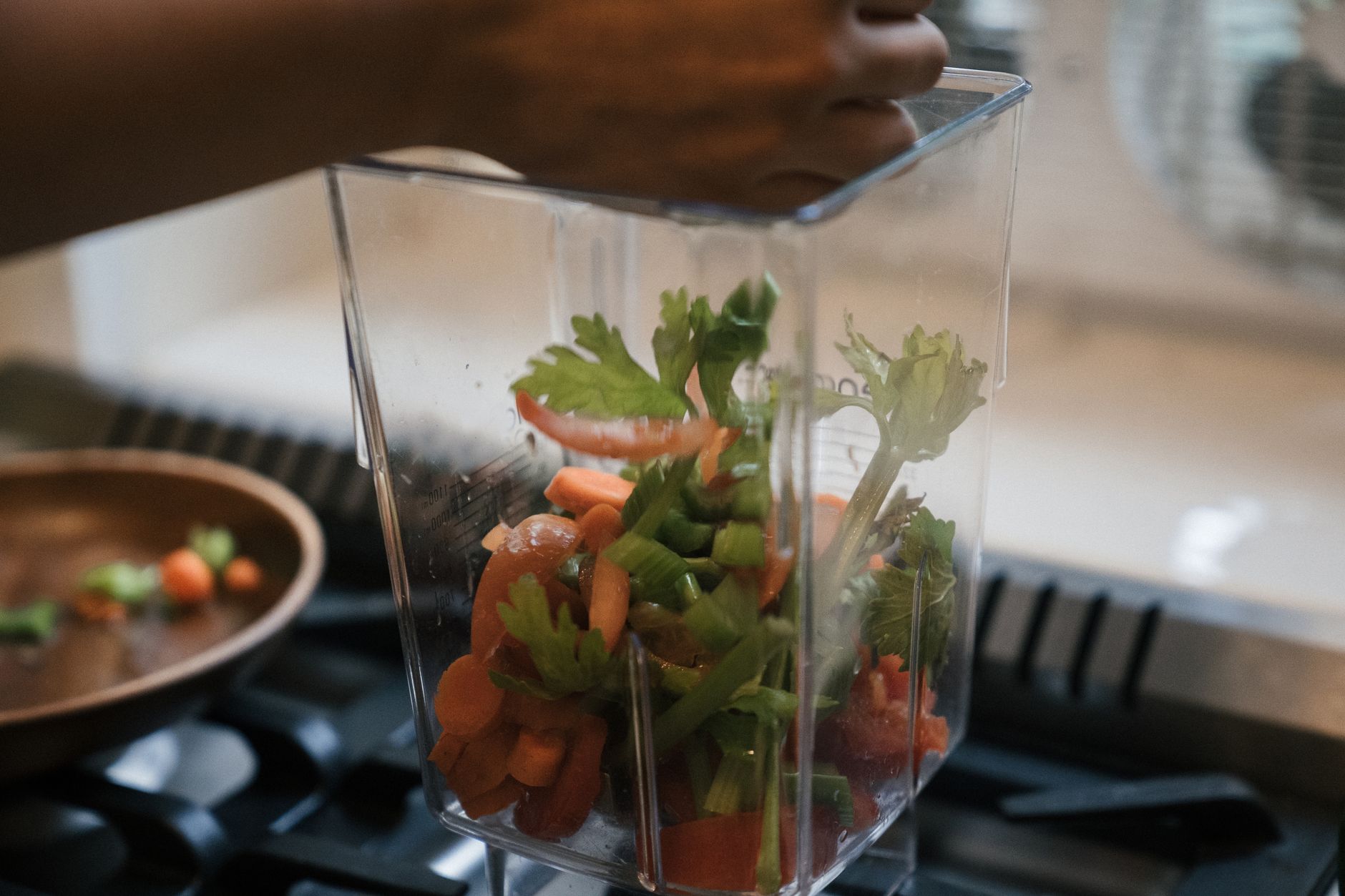Close-up of fresh vegetables being placed in a blender in an indoor kitchen setting.