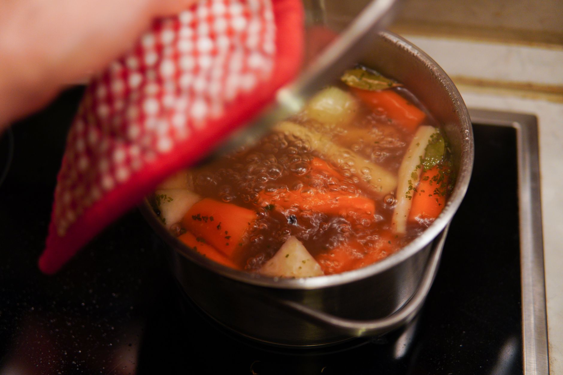 A person cooking vegetable soup with fresh carrots and herbs indoors.