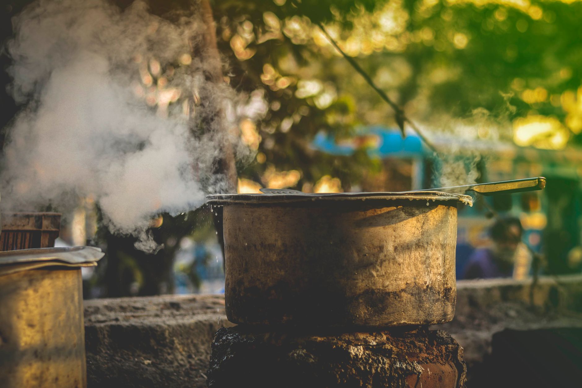 Rustic outdoor cooking pot steaming on a stove at sunset, creating a warm, atmospheric scene.